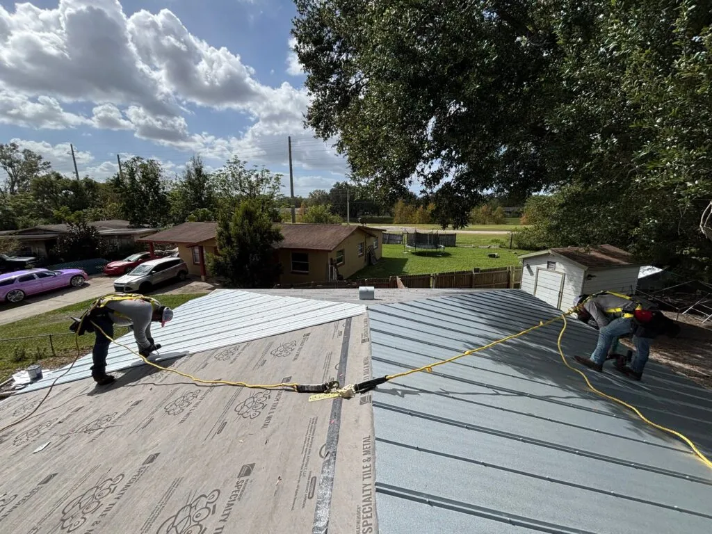 new metal roof being installed by two royalty workers with harnesses attached to middle of roof