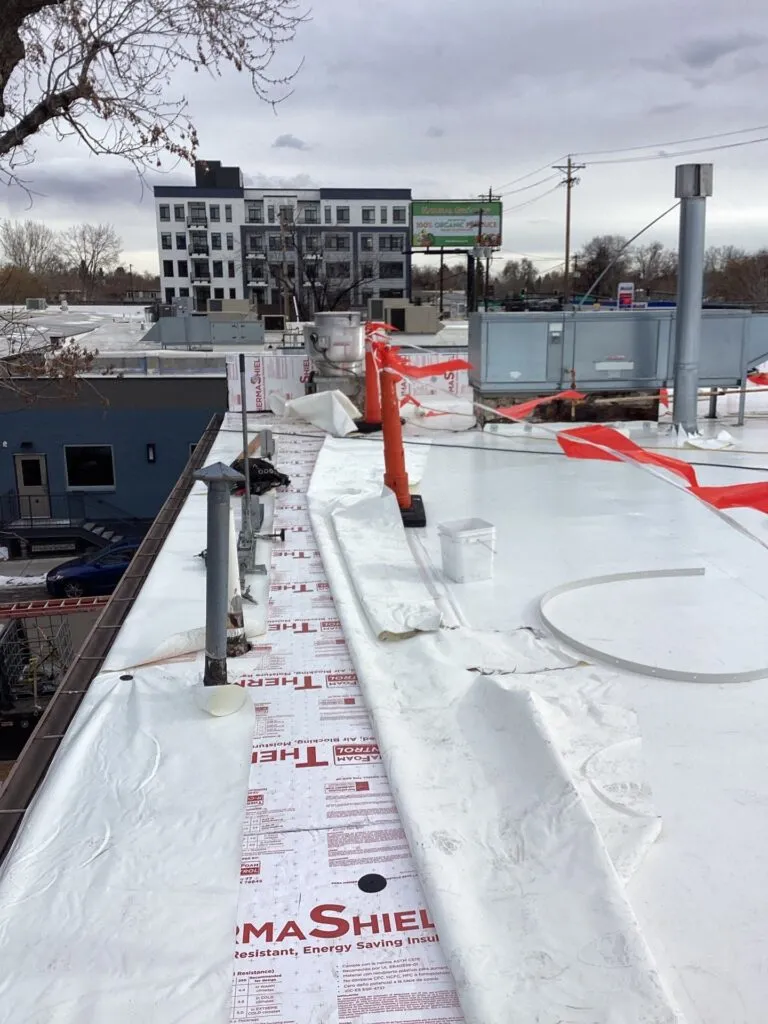 flat roof in process of replacement with safety orange flags and insulation showing as its covered by shite single-ply pvc sheets