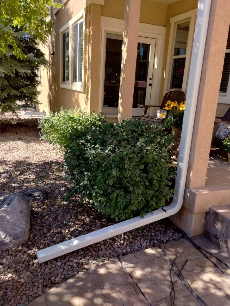 white downspouts installed on stucco home in colorado showing how water is let out into river rock by home
