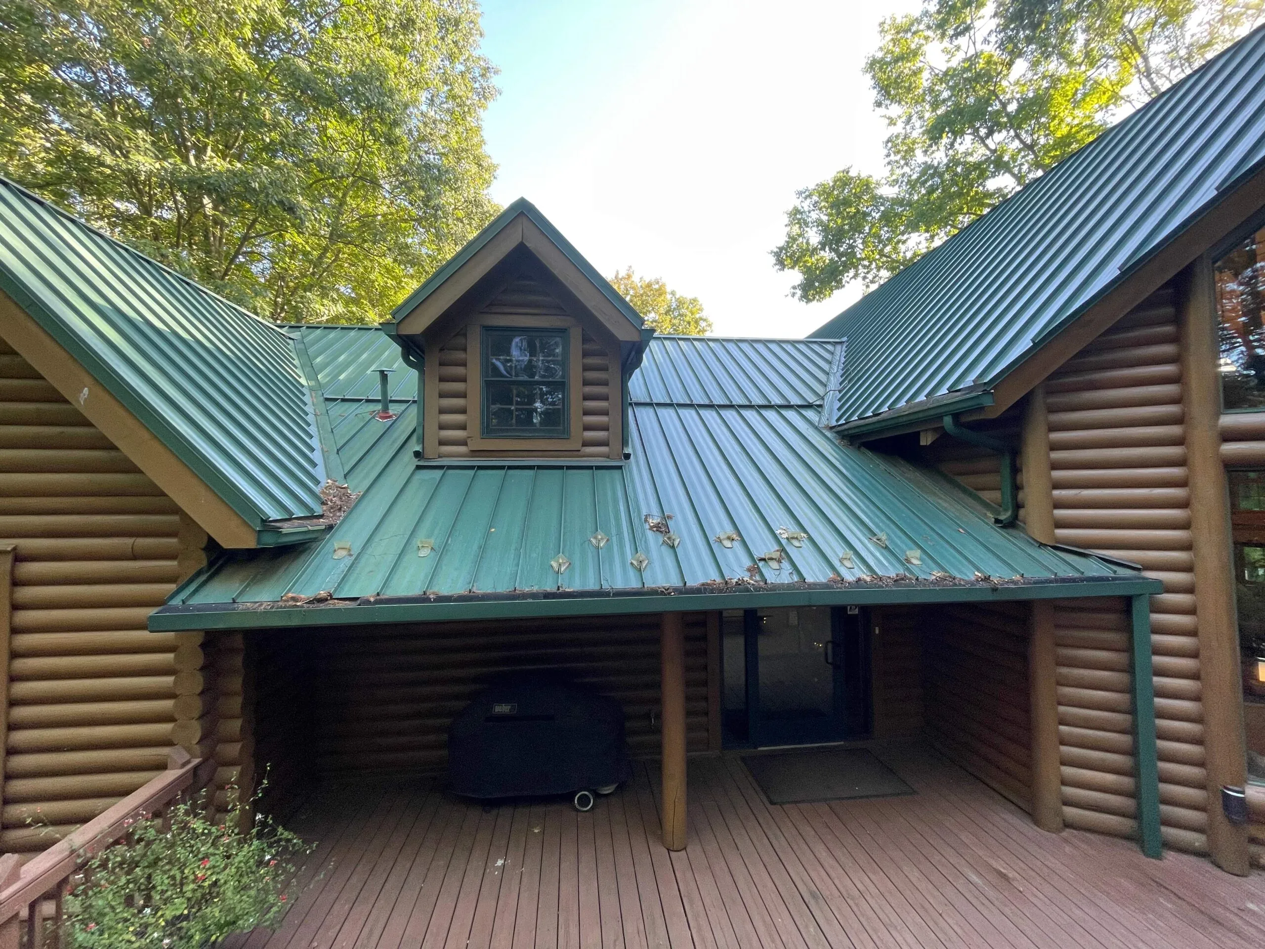 green metal roof on cabin in need of repair with leaves in gutter