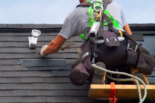 close up of man nailing in shingle tiles on roof
